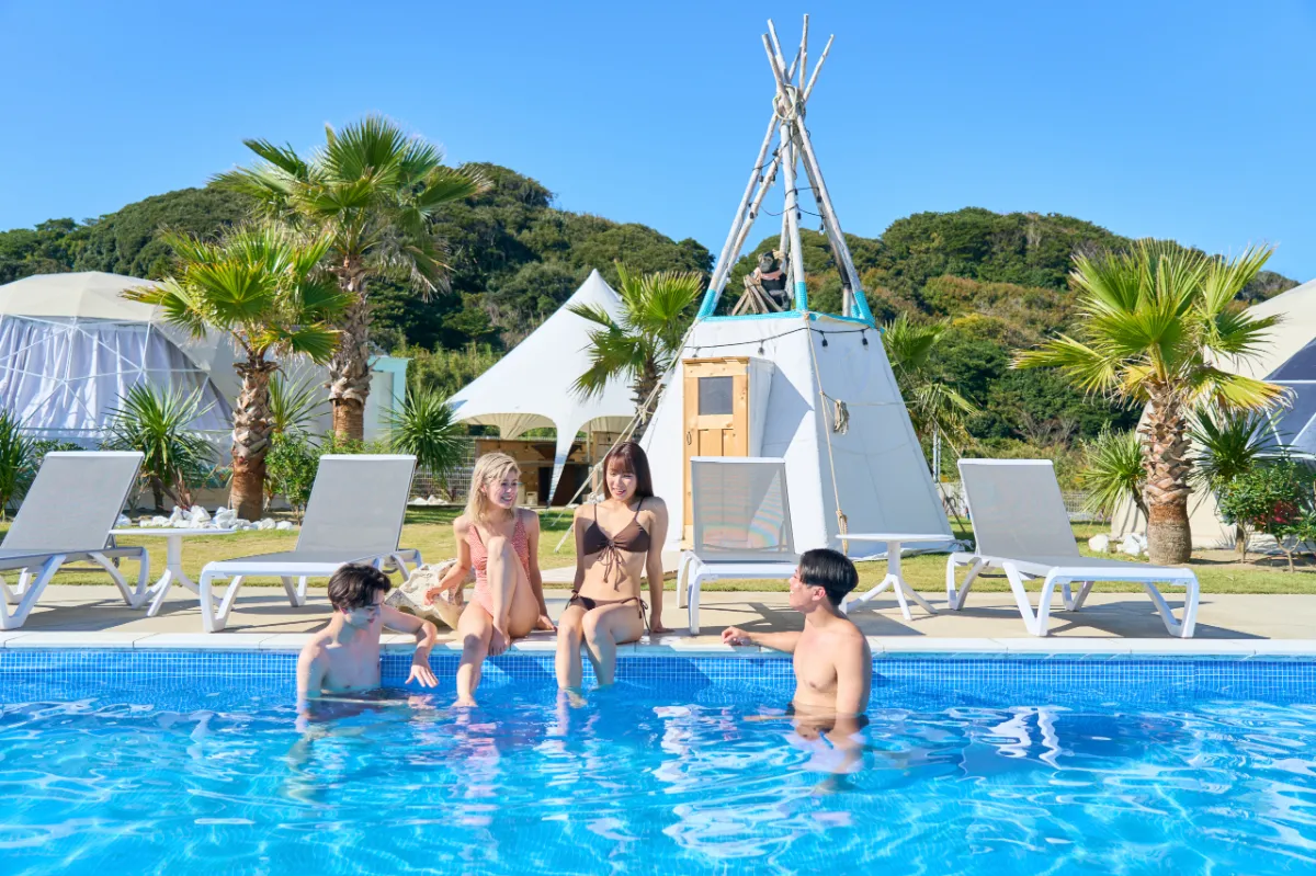 水辺で語らう、OASIS-OARAIの晴れやかなひととき - 茨城・大洗ひたちなかエリアのグランピング施設 Water front Villa OASIS大洗 OASIS-OARAIのプールで4人のゲストが水辺で会話とリラックスを楽しんでいる様子。