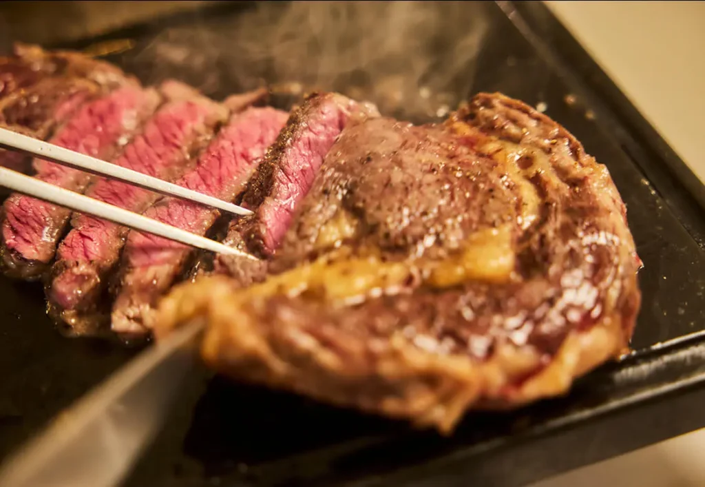 鉄板の上で焼きたてのステーキをカットする様子。湯気が立ち上るジューシーな断面。