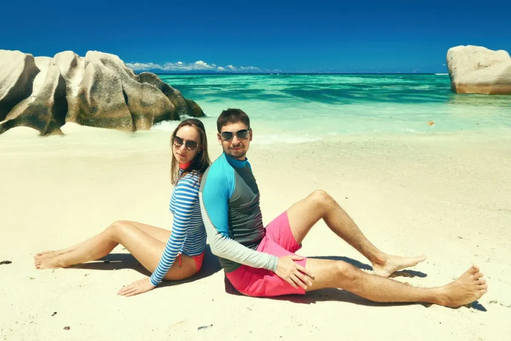 海辺で過ごすラッシュガードスタイル - 茨城・大洗ひたちなかエリアのグランピング施設 Water front Villa OASIS大洗 海辺でラッシュガードとサングラスを着用して座る二人の様子