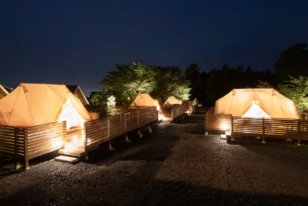 ETOWA KASAMA|夜のライトアップされたテントエリア - 茨城・大洗ひたちなかエリアのグランピング施設 Water front Villa OASIS大洗 ETOWA KASAMAの夜のグランピングテントエリア。ライトアップされたテントと木製デッキが並ぶ静かな森の風景